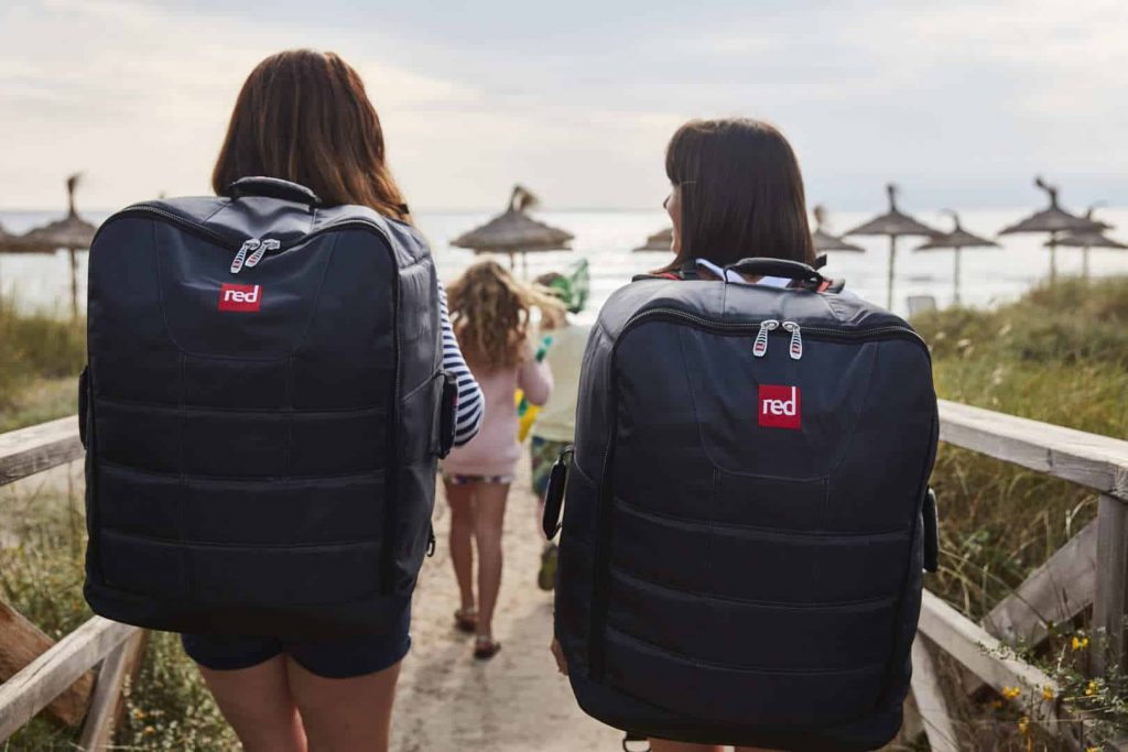 Chicas transportando una tabla de paddle surf hinchable en la mochila.
